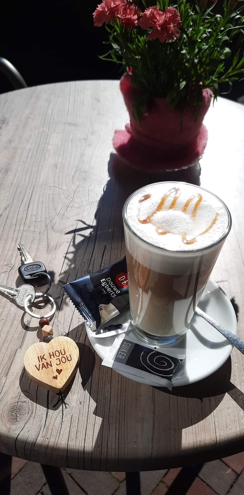 Een glas koffie met melkschuim op een tafeltje buiten